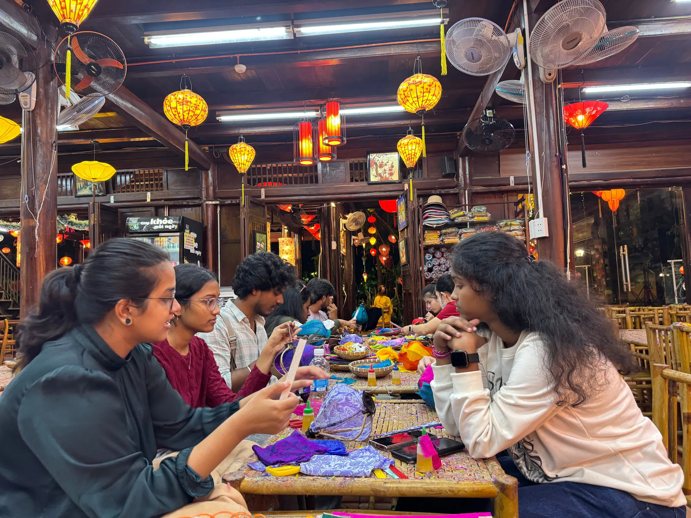 Students making traditional lanterns at a table under hanging lanterns