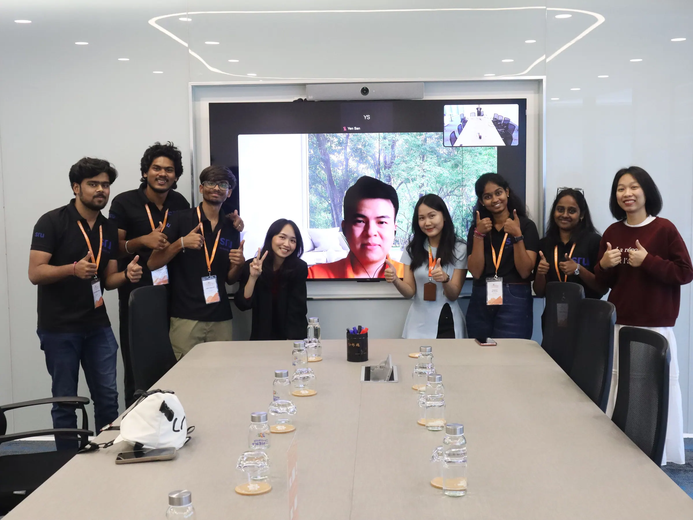 The group in a meeting room with a speaker on the video screen behind them